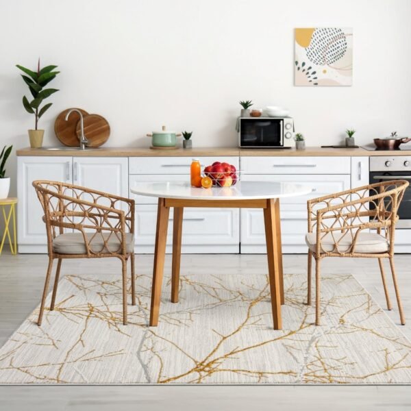 Dining area with a modern gold-accented abstract rug featuring a tree branch design, paired with a round wooden table and rattan chairs, set in a minimalist kitchen.