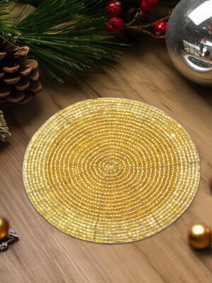 A festive table setting featuring a gold beaded coaster, surrounded by holiday decor including candles, pinecones, and ornaments.