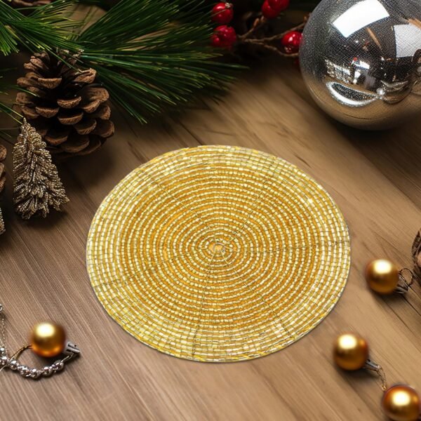 A festive table setting featuring a gold beaded coaster, surrounded by holiday decor including candles, pinecones, and ornaments.