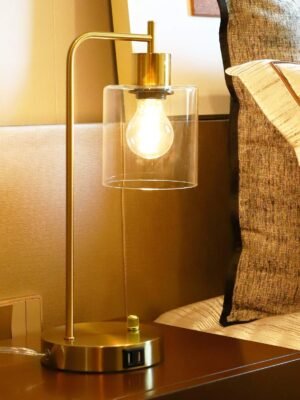 Gold industrial table lamp featuring a clear glass shade, modern design, and two USB ports for convenient device charging, paired with a sleek gold base